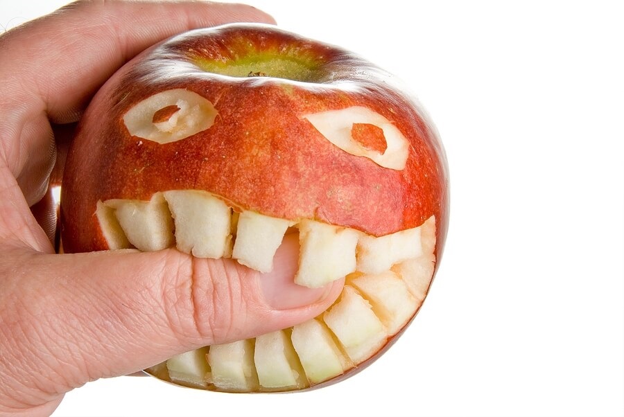 Funny face carved into apple, biting thumb against white back drop.