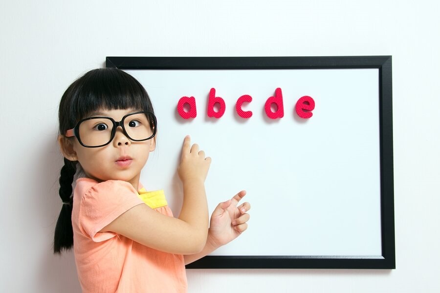 Little girl in glasses standing in front of white board with magnetic letters.